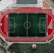 An aerial view of a large sports complex featuring a central green football field surrounded by a red running track. Adjacent to the track, there is a parking area, buildings, and pathways. Nearby, there are additional sports courts in different colors, including a blue swimming pool and orange basketball courts.